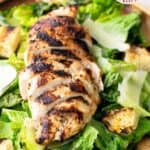 Sliced grilled chicken breast served on romaine lettuce with croutons and shaved parmesan cheese, labeled as “grilled chicken caesar salad.”.