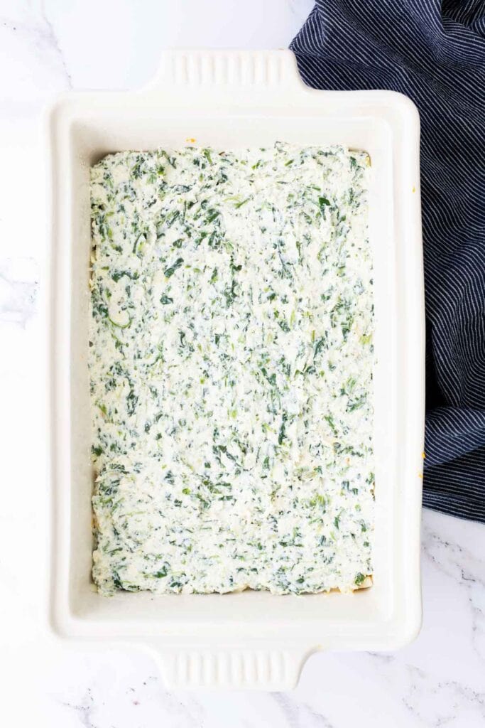 Rectangular casserole dish filled with a creamy spinach mixture, topped with a blue and white striped cloth partially visible in the corner.
