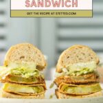Two fried green tomato po’ boy sandwiches with lettuce and sauce on a white plate, sitting on a light surface.
