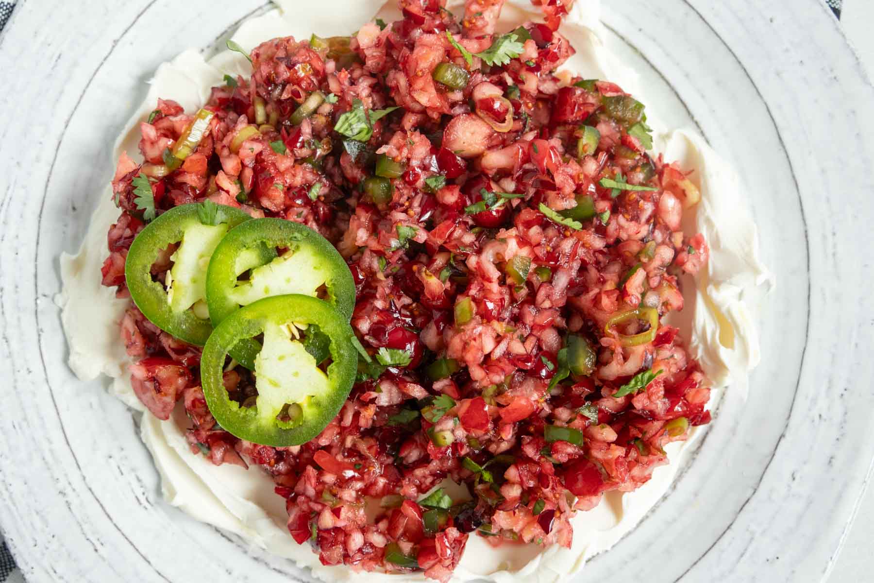 Cranberry jalapeño salsa served over a mound of cream cheese, garnished with fresh jalapeño slices.