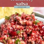 A bowl of cranberry salsa served with tortilla chips, with the text “cranberry salsa” overlaid at the top.