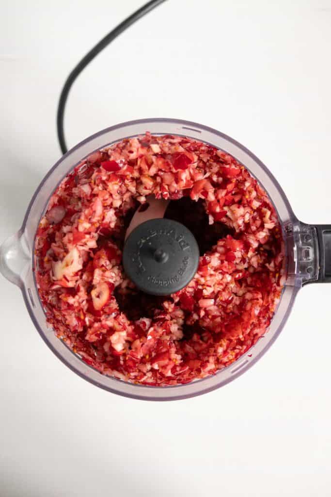 Top-down view of a food processor bowl filled with finely chopped red cranberries.