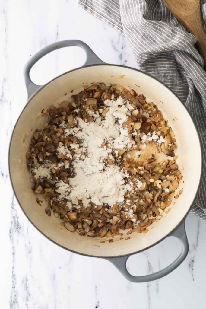 A dutch oven containing sautéed mushrooms and onions topped with a dusting of flour.