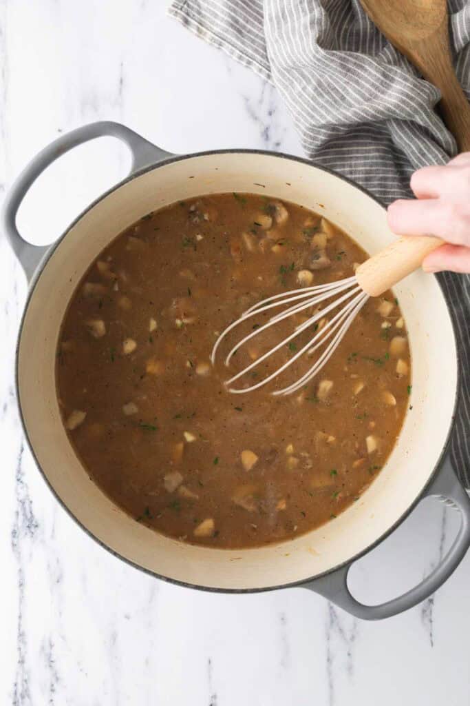 A hand whisks mushroom gravy in a large pot.