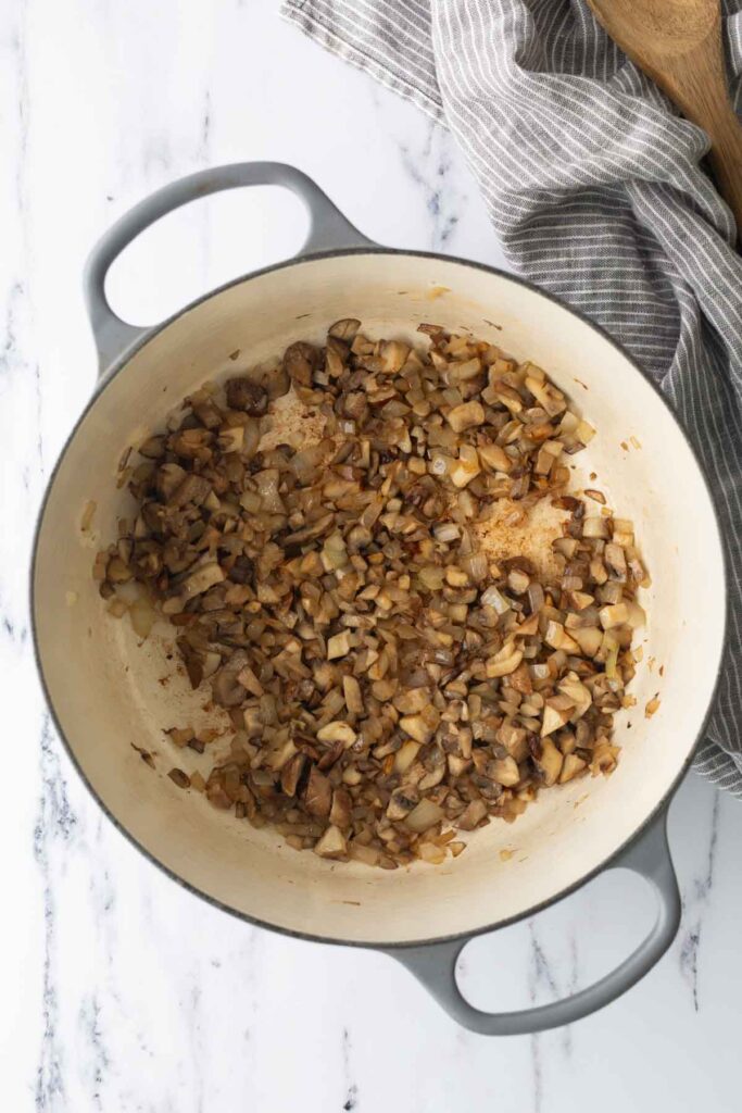 Diced onions and mushrooms sautéing in a Dutch oven.