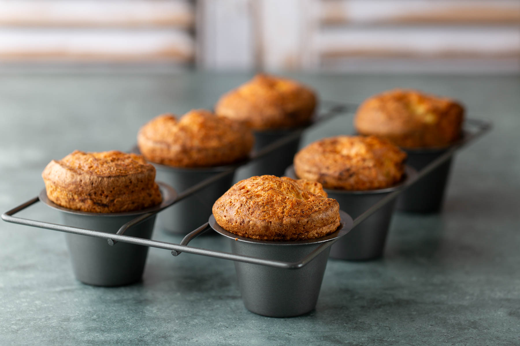Six golden-brown popovers in a metal baking pan.