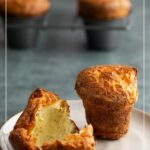 Black pepper parmesan popovers, one torn open on a plate, with more in a baking tin behind.
