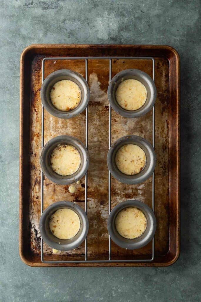 Six baked egg bites in a metal muffin pan on a baking sheet.