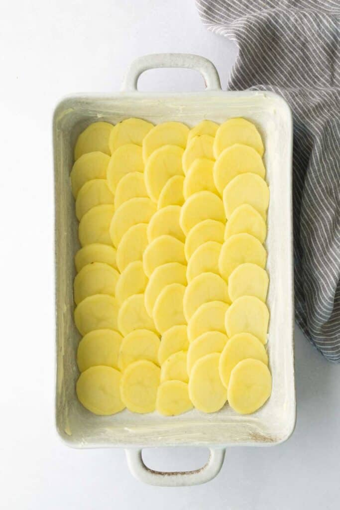 Thinly sliced raw potatoes layered in a rectangular baking dish.