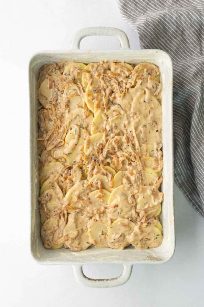 A rectangular baking dish filled with thinly sliced potatoes covered in a creamy onion sauce.